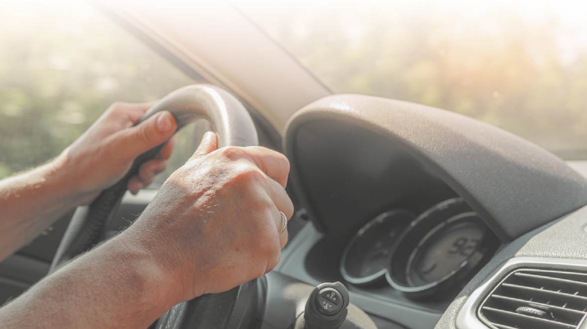 Fotografia das duas mãos de uma pessoa segurando o volante enquanto dirige.