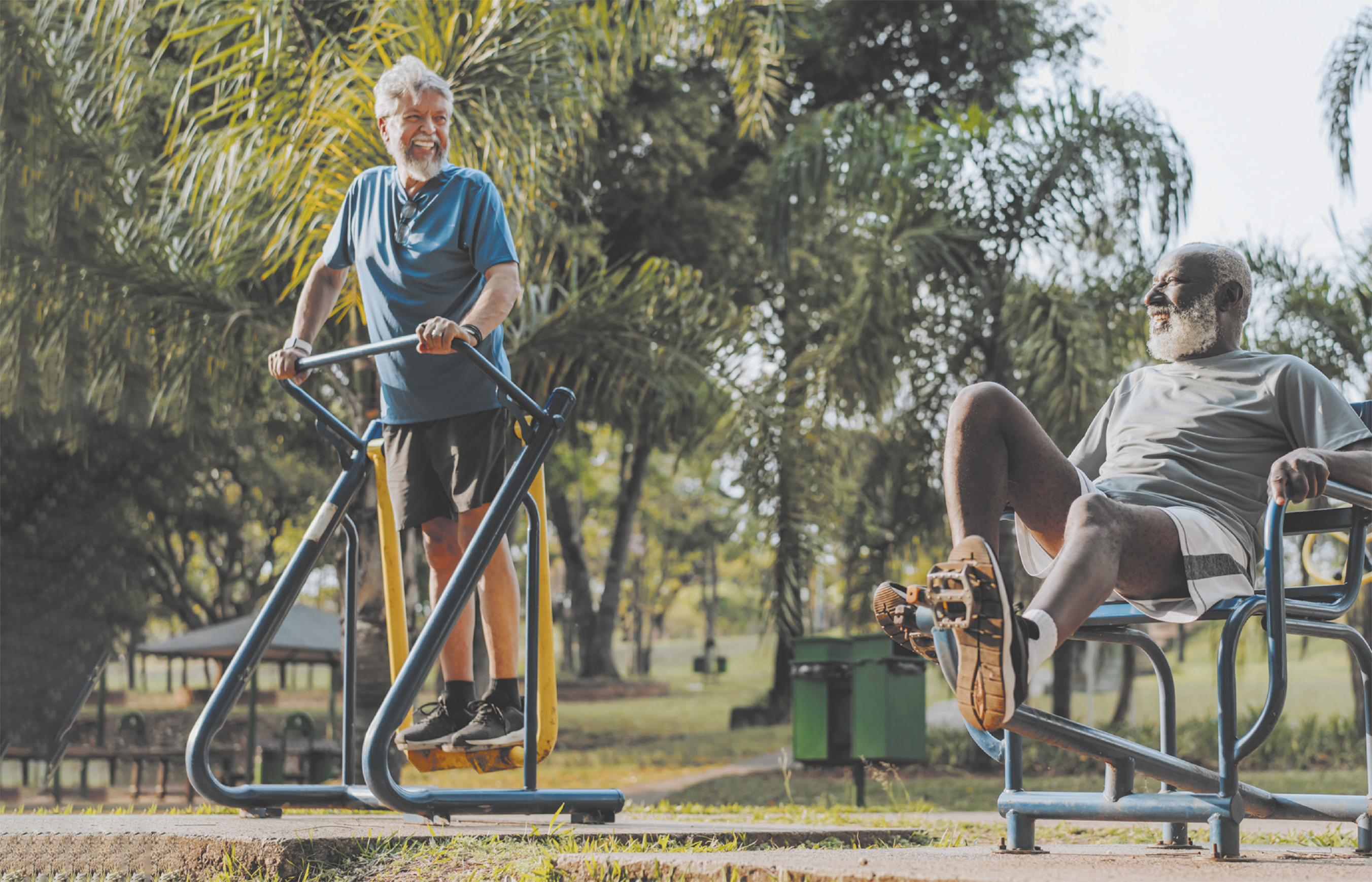 Fotografia de dois homens idosos utilizando equipamentos de ginástica em um parque.