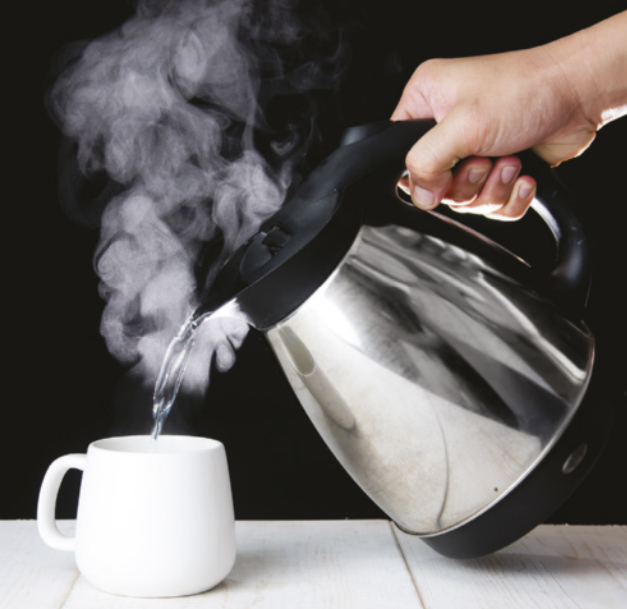 Fotografia de mão de pessoa despejando água quente de uma garrafa térmica em uma xícara.