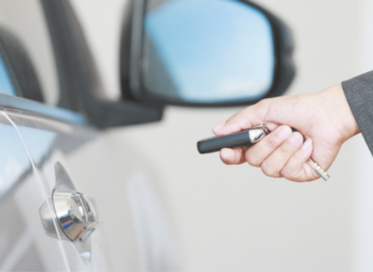 Fotografia de mão segurando um dispositivo em direção à porta de um carro.