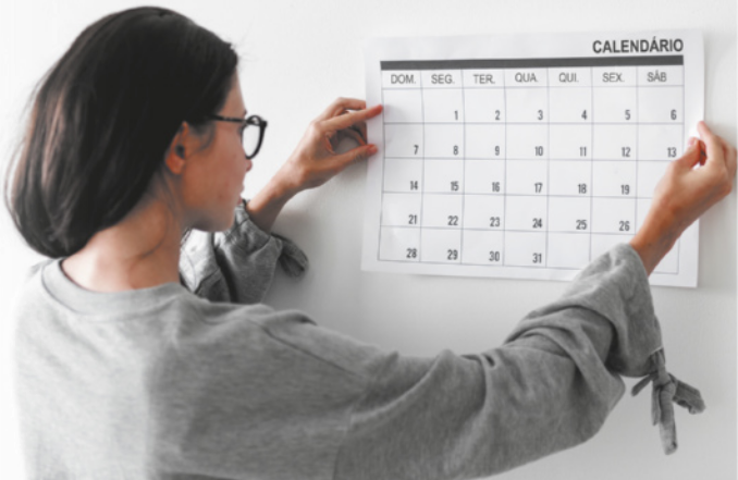 Fotografia de mulher colocando um calendário na parede.