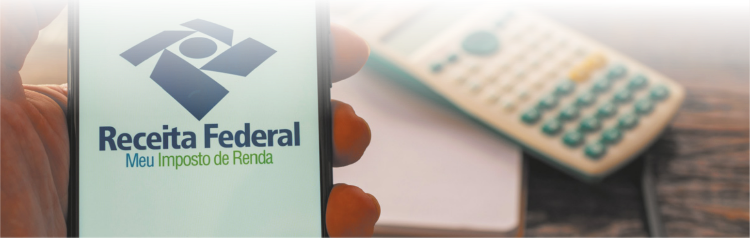 Fotografia de mão segurando um celular em cuja tela está escrito Receita Federal Meu Imposto de Renda.