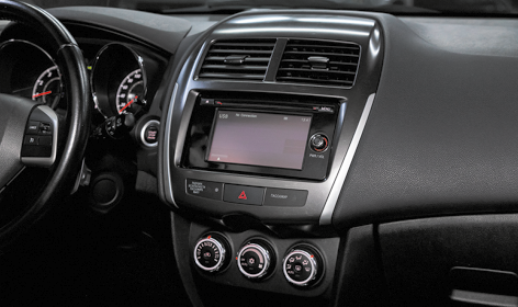 Fotografia do painel de um carro, evidenciando o console central e parte do volante à esquerda. O painel é predominantemente preto, com detalhes em prata ao redor das saídas de ar e da central multimídia.