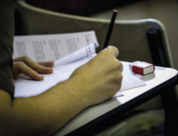 Foto de estudante escrevendo em uma prova.
