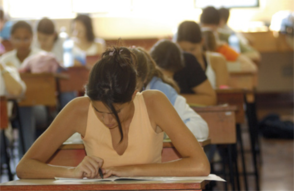Foto de estudantes em uma sala de aula. Eles estão escrevendo redações.