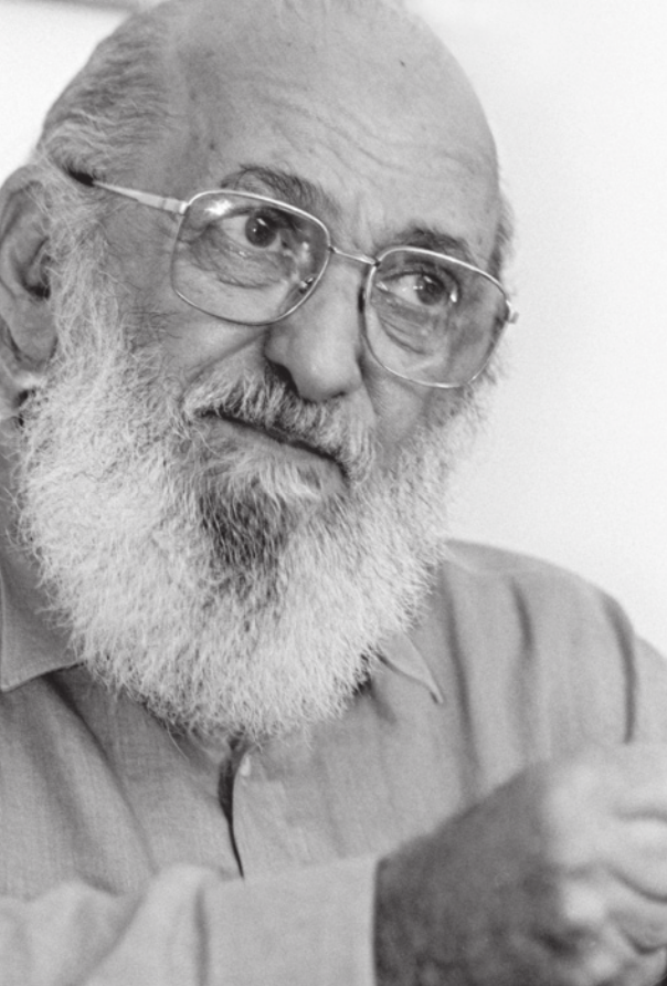 Foto de Paulo Freire. Ele possui barba, é calvo e usa óculos.