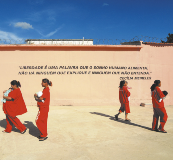 Foto de mulheres usando uniformes. Elas estão em um pátio, segurando bebês. No muro do pátio está escrito 'Liberdade é uma palavra que o sonho humano alimenta. Não há ninguém que explique e ninguém que não entenda. Cecília Meirelles'.