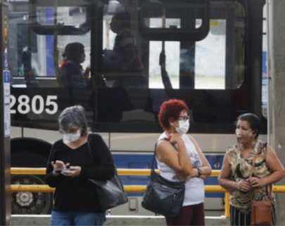 Foto de mulheres em um ponto de ônibus. Elas usam máscaras de proteção.
