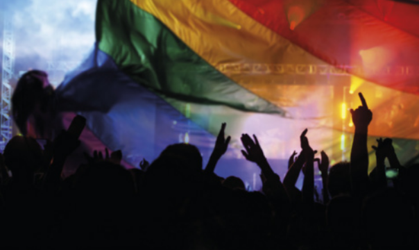 Foto de pessoas reunidas sob uma bandeira do arco-íris.