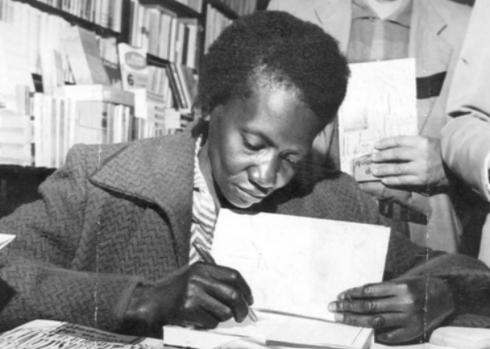 Foto de Carolina Maria de Jesus autografando seu livro. Ela é uma mulher negra e possui cabelos curtos.
