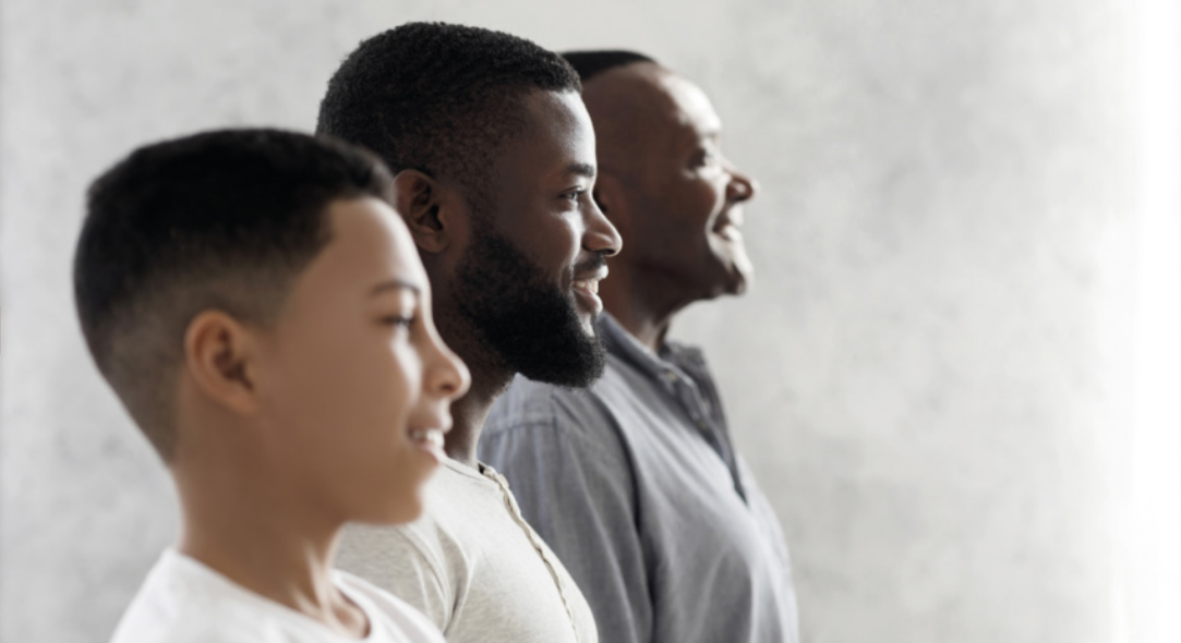 Imagem de um homem, um jovem e um menino lado a lado. Eles estão de perfil, sorrindo.