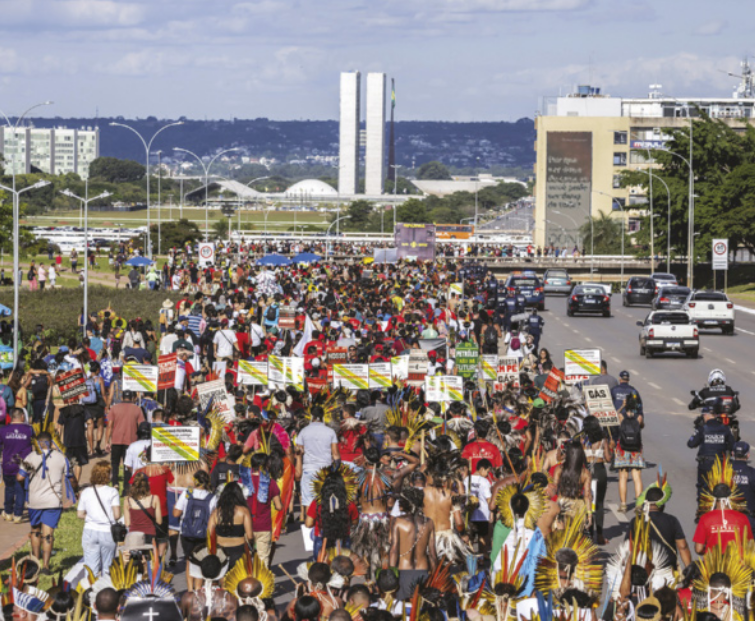 Imagem de manifestantes indígenas caminhando em direção ao edifício do Congresso Nacional.