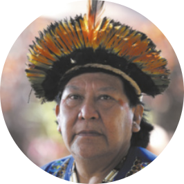 Fotografia de Davi Kopenawa. Ele é indígena, idoso e usa cocar.