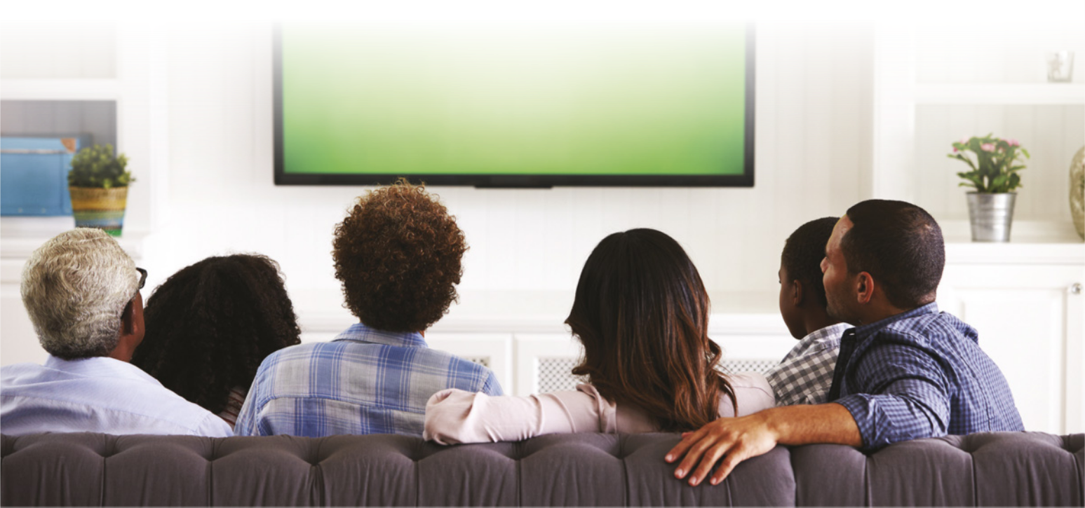Imagem de família sentada em um sofá, assistindo televisão.
