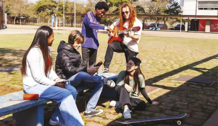 Imagem de grupo de jovens em uma praça. Uma garota negra está sentada em um banco, ao lado de um garoto branco, que utiliza um celular e um fone de ouvido. Perto dele, uma garota asiática está sentada no chão, ao lado de um skate. Atrás dela, há um garoto negro sorrindo e um garoto ruivo tocando guitarra.
