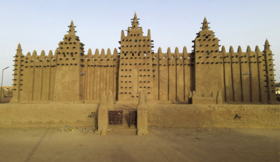 Imagem de mesquita com três torres quadrangulares. Há espinhos ao longo das paredes da fachada e o portão de entrada situa-se entre muros com pilares pontiagudos.