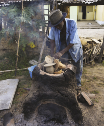 Imagem de artesão negro queimando recipientes de argila em um forno ao ar livre.