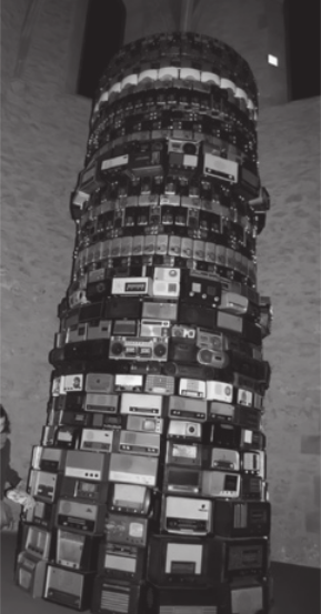Imagem em preto e branco de instalação artística. Ela possui diversos rádios portáteis empilhados, formando uma torre arredondada.