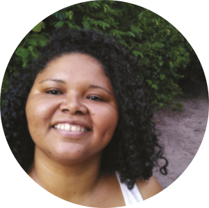 Fotografia de Ana Mumbuca. Ela é negra, possui cabelos cacheados e está sorrindo.