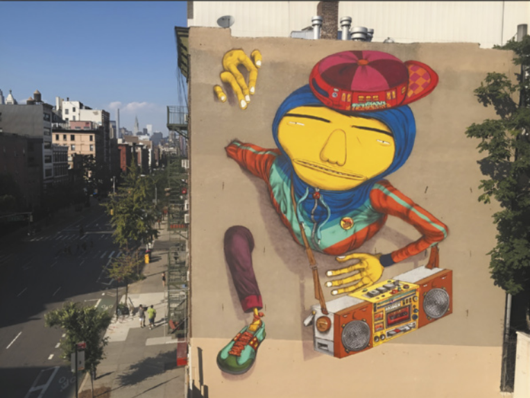 Imagem de grafite na lateral de um prédio. O grafite representa um homem atravessando a parede, com um aparelho de som pendurado por uma correia no ombro direito. Ele usa tênis, calça, agasalho com capuz e boné com a aba virada para trás. O quadril, a perna esquerda e o cotovelo direito estão ocultos na parede.