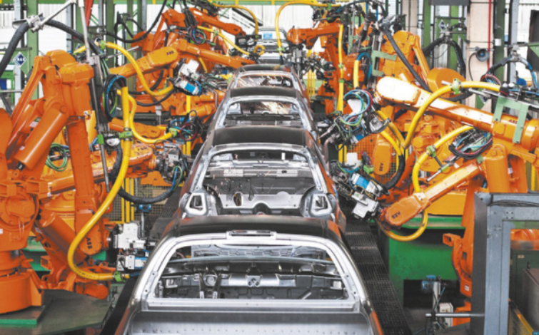 Imagem de fábrica de automóveis. Carrocerias estão dispostas em fila, entre braços mecânicos.