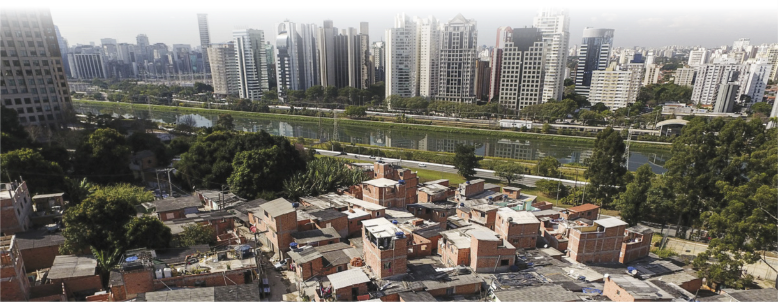 Imagem aérea de um rio em uma cidade urbanizada. Na margem esquerda do rio, há moradias populares. A margem direita contém diversos edifícios de luxo.