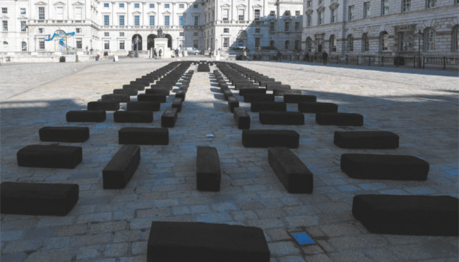 Instalação artística com blocos retangulares enfileirados em uma praça pavimentada.