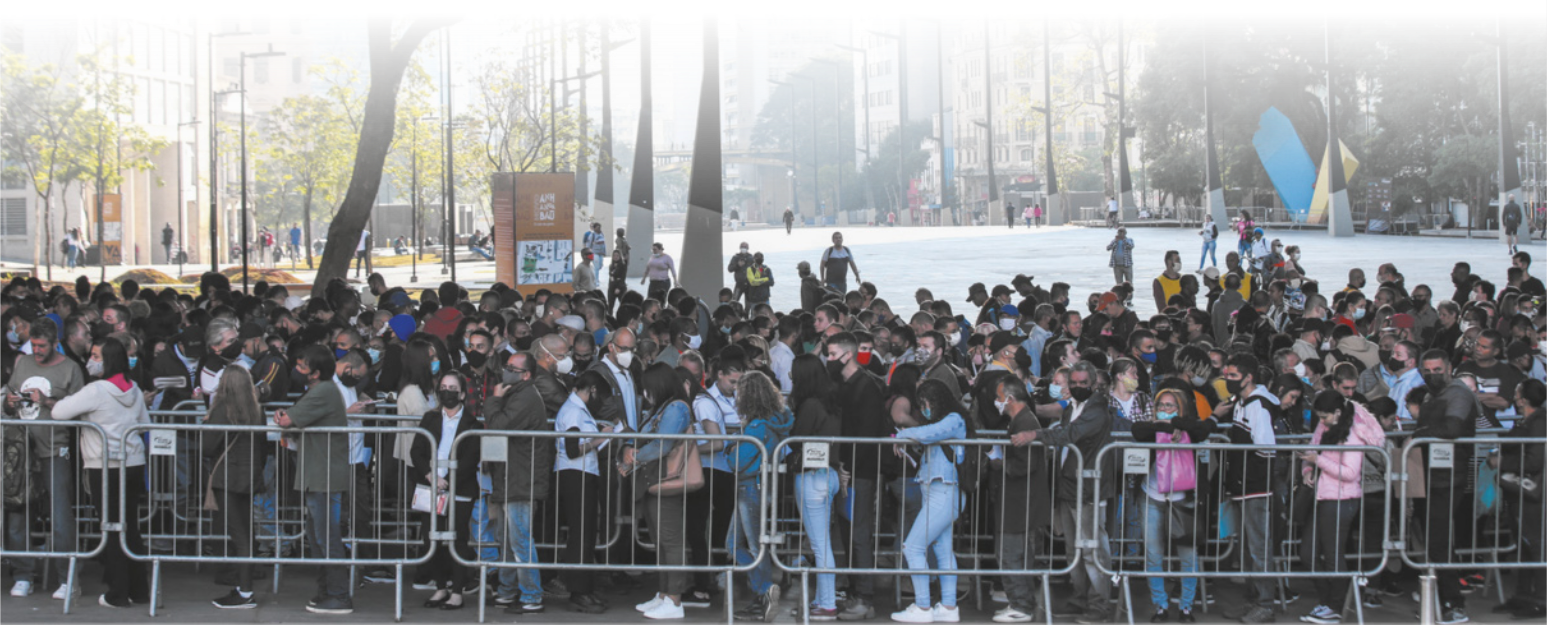 Imagem de pessoas enfileiradas em uma praça. A fila se estende ao longo de corredores delimitados por grades.