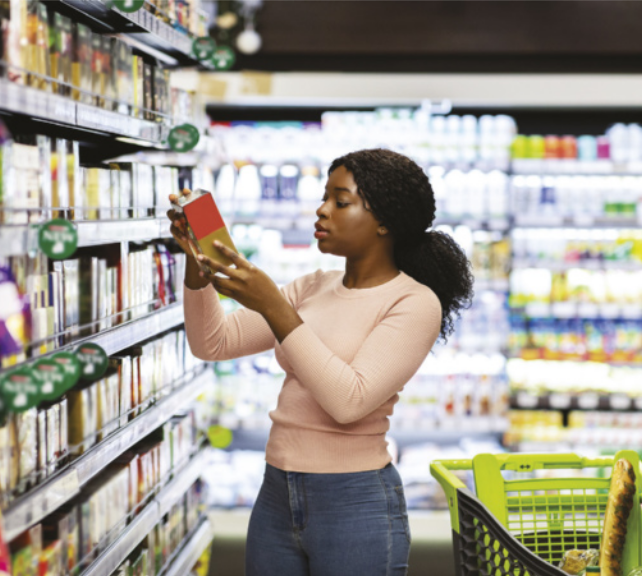 Imagem de mulher em um supermercado, lendo o rótulo de uma embalagem.