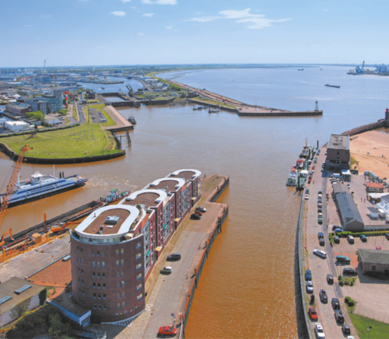 Imagem de rio desaguando no mar. O rio flui por meio de dois canais cercados por edifícios e vias pavimentadas.
