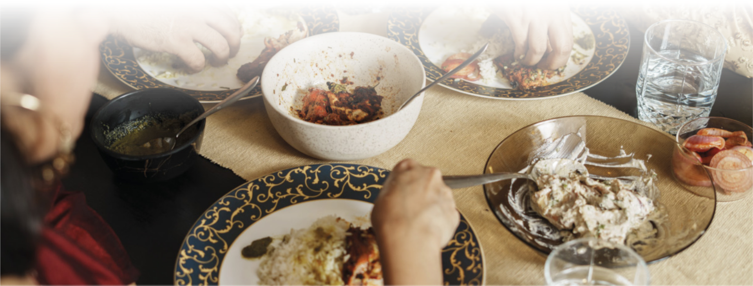 Imagem de pessoas fazendo uma refeição. Elas comem arroz e frango com as mãos em pratos com borda decorada.