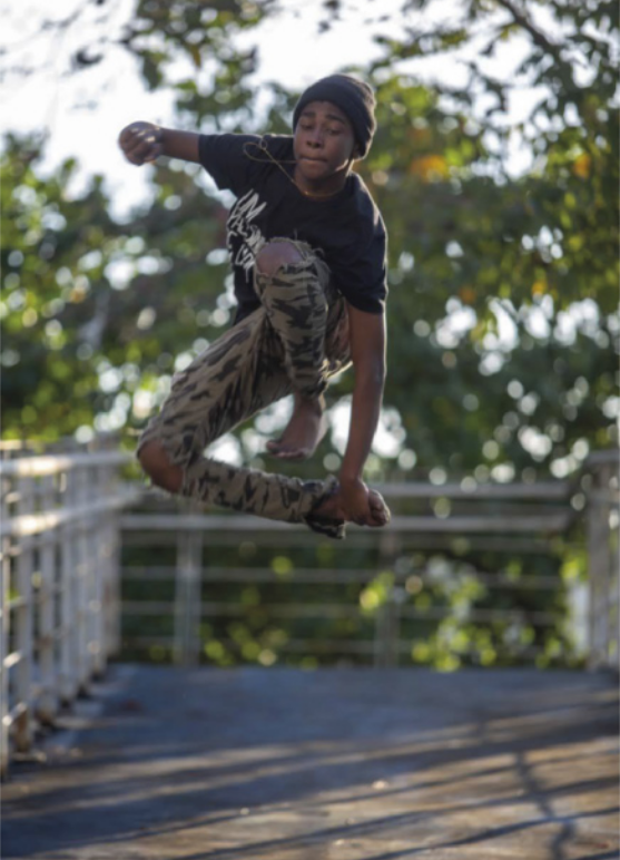Imagem de Lipinho da Costa executando um passo de dança. Ele salta, segura o tornozelo direito e passa o pé esquerdo sobre a perna.