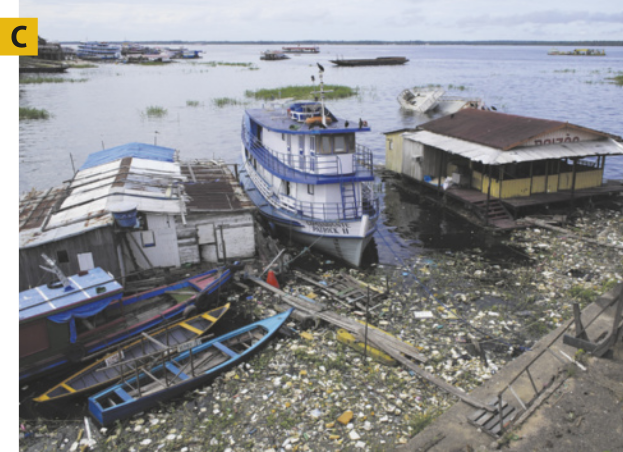 C. Fotografia de barcos abandonados e lixo em um rio. Além disso, há algumas construções em cima de deques.