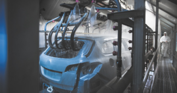 Fotografia de uma máquina realizando um procedimento de pintura da carroceria de um carro.