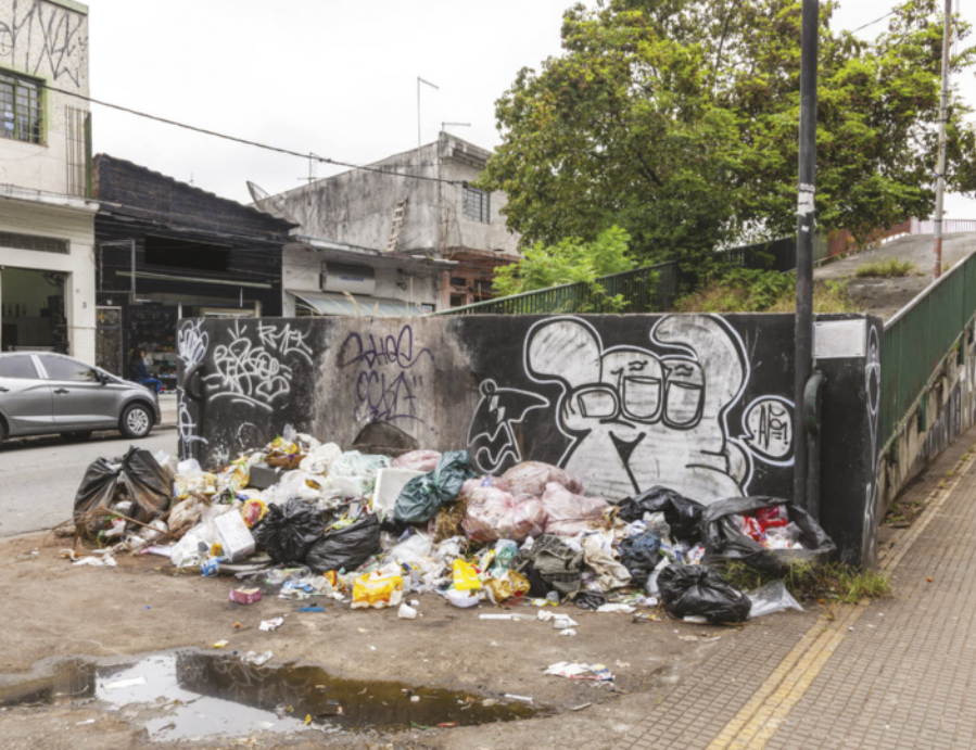Fotografia de uma pilha de lixo jogada em frente a um muro em um centro urbano.