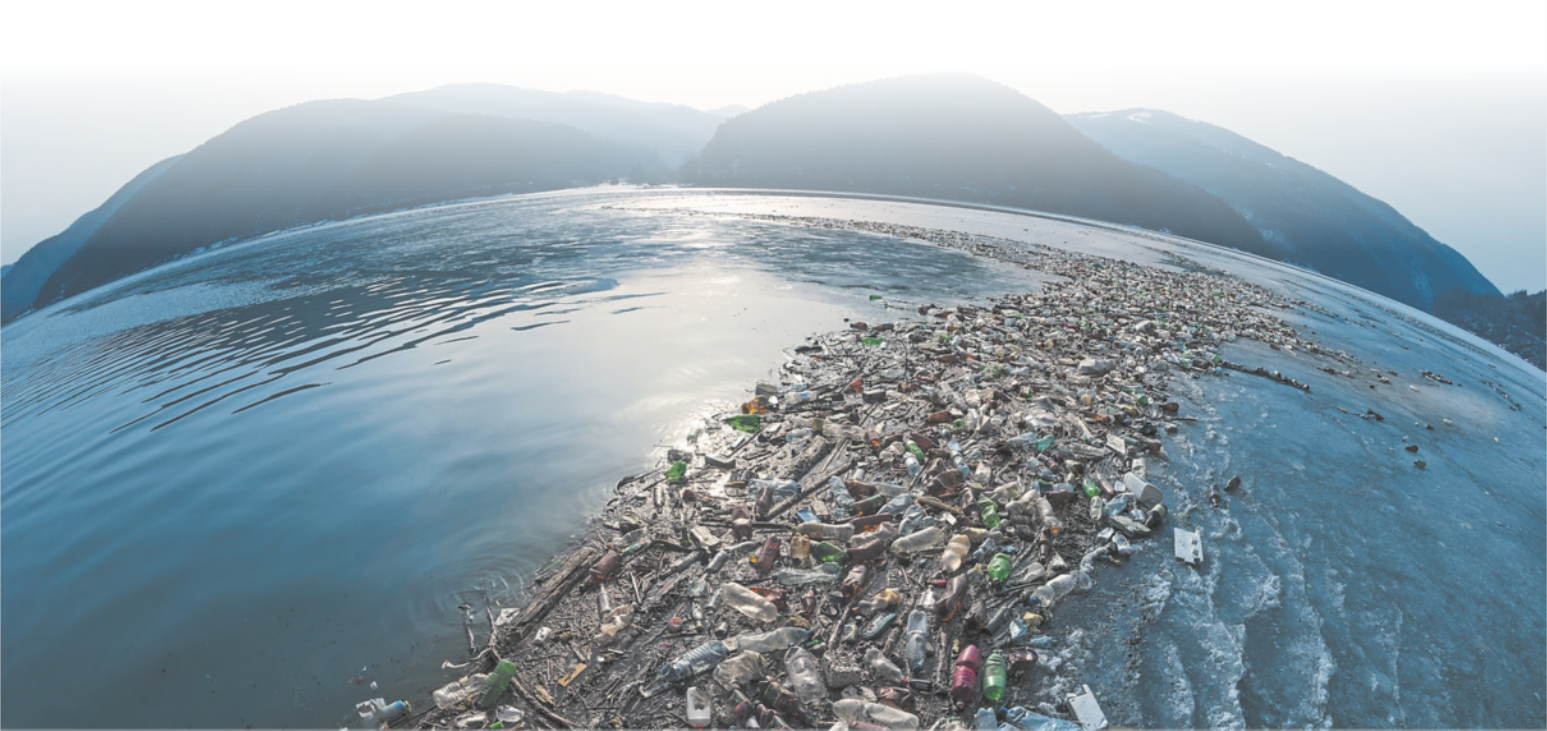 Fotografia de trilha de plástico flutuando no mar. Ao fundo, há montanhas.