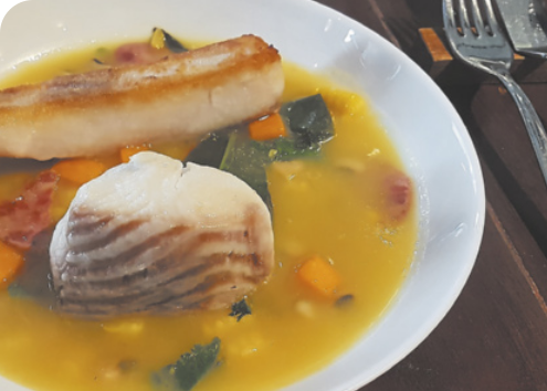 Fotografia de um prato de peixe no tucupi. Há um pedaço de peixe envolvido em um caldo amarelo com legumes e verduras.