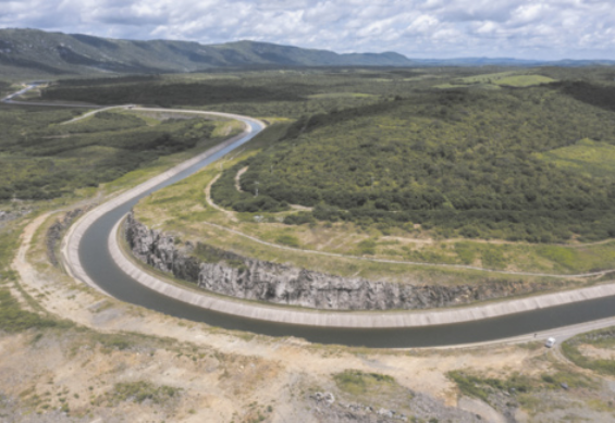 Fotografia aérea do Rio São Francisco. O rio é tortuoso e possui ambas as margens concretadas. Há vegetação de ambos os lados do rio, e montanhas ao fundo.