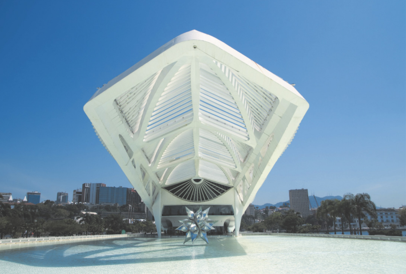 Fotografia de um edifício com estrutura metálica branca em formato de pentágono, com uma cidade ao fundo.