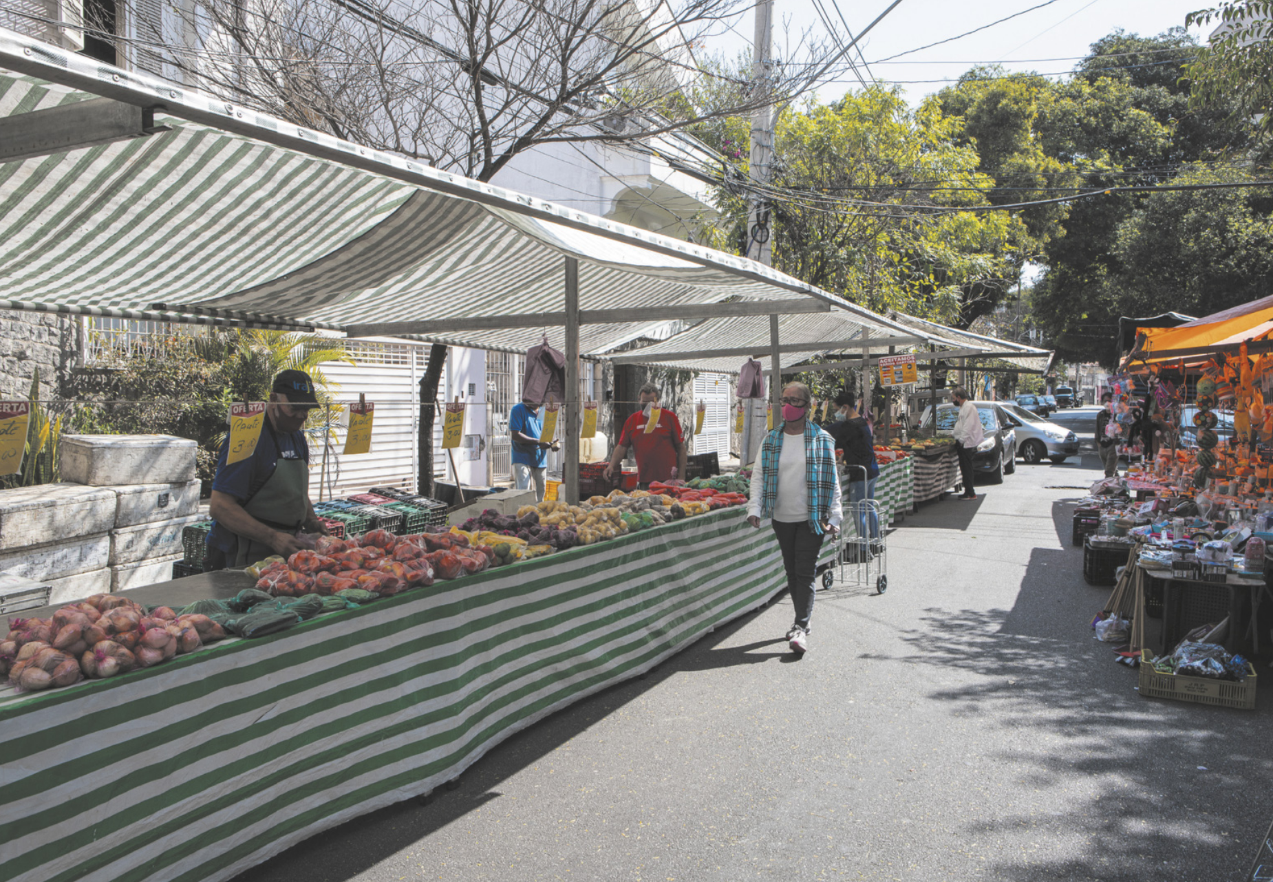Fotografia de uma feira livre, com barracas de frutas e legumes e pessoas circulando com máscaras de proteção.