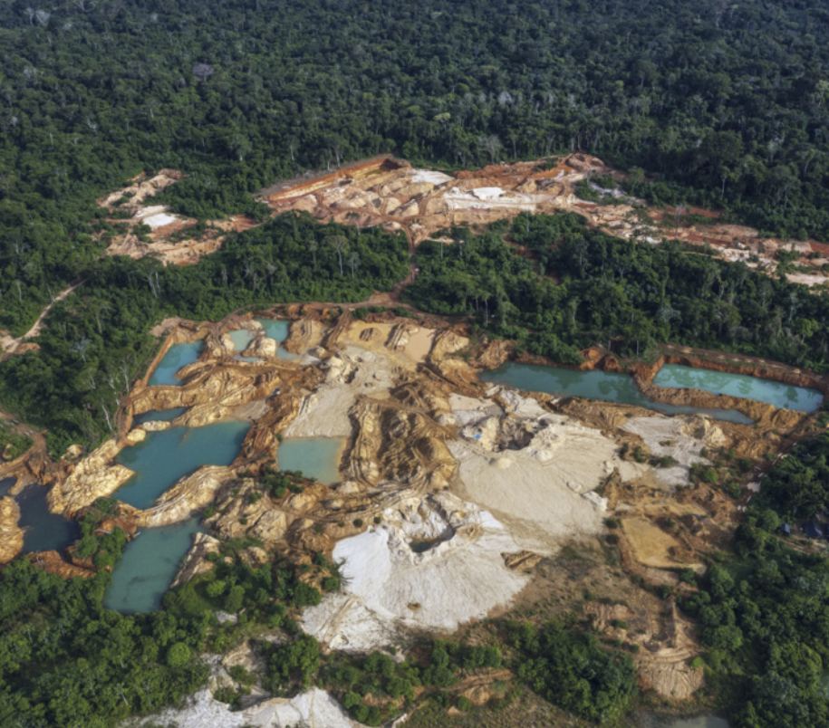 Fotografia aérea de uma área de floresta com uma grande extensão desmatada, onde há escavações e água represada. Ao fundo, observa-se a vegetação densa preservada.