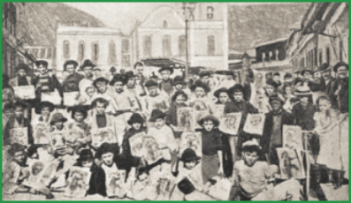 Fotografia em preto e branco que mostra dezenas de crianças posando para a câmera, cada uma segurando a primeira página de jornais. Elas estão posicionadas no meio da rua, com edifícios antigos ao fundo.