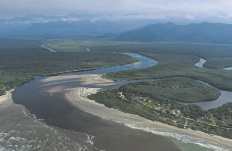 Fotografia de um rio extenso e sinuoso que atravessa uma área de floresta densa. Ao fundo, observa-se uma cadeia de montanhas coberta por vegetação.