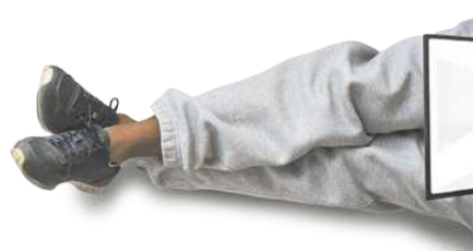 Imagem das pernas de uma pessoa sentada no chão, esticadas, segurando um notebook.