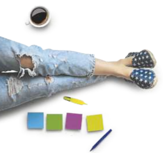 Imagem da perna de uma pessoa sentada no chão, esticada, ao lado de uma xícara de café, blocos de anotações e canetas.