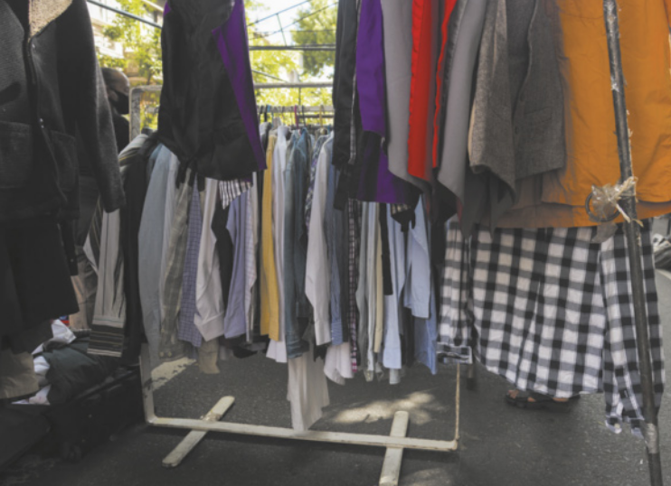 Fotografia de roupas organizadas em araras. Há diversos tipos de camisas penduradas em cabides expostos.