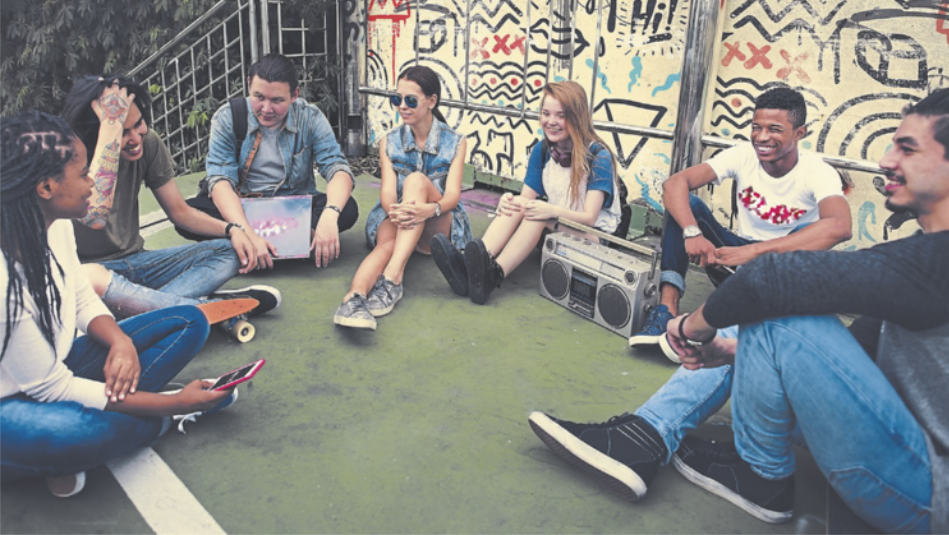 Fotografia de jovens reunidos sentados no chão, em roda, conversando. Atrás deles, há uma parede com grafites desenhados e eles escutam um aparelho de som.