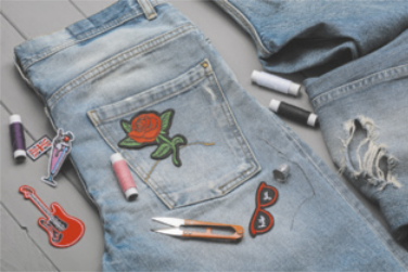 Fotografia de uma calça jeans dobrada com o bolso à mostra. No bolso, há a imagem de uma rosa vermelha costurada e linhas de costura ao redor.