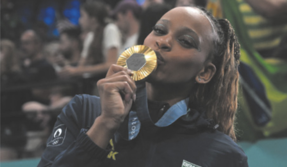 Fotografia de Rebeca Andrade. Ela é uma menina negra e está com os cabelos presos, beijando uma medalha olímpica de ouro.