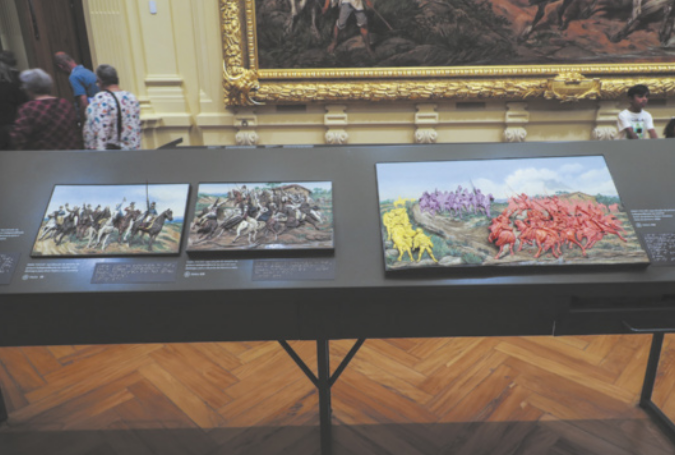Fotografia do interior de um museu com uma mesa contendo uma reprodução tátil de dois quadros, um ao lado do outro.